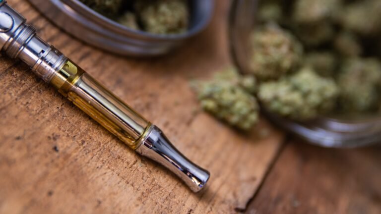 Cannabis Oil Vape Pen & Marijuana Buds In Open Glass Jar In Background