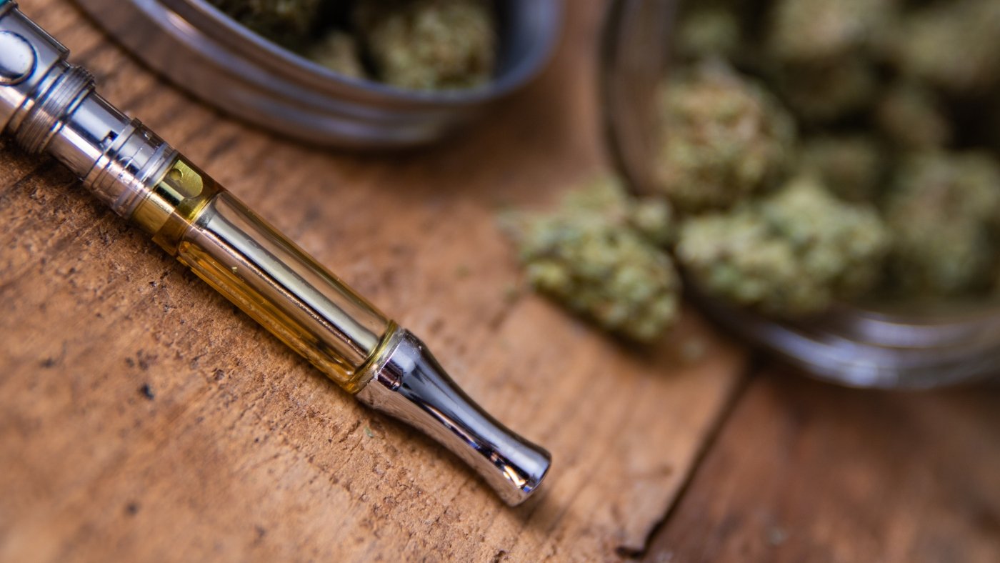 Cannabis Oil Vape Pen & Marijuana Buds In Open Glass Jar In Background